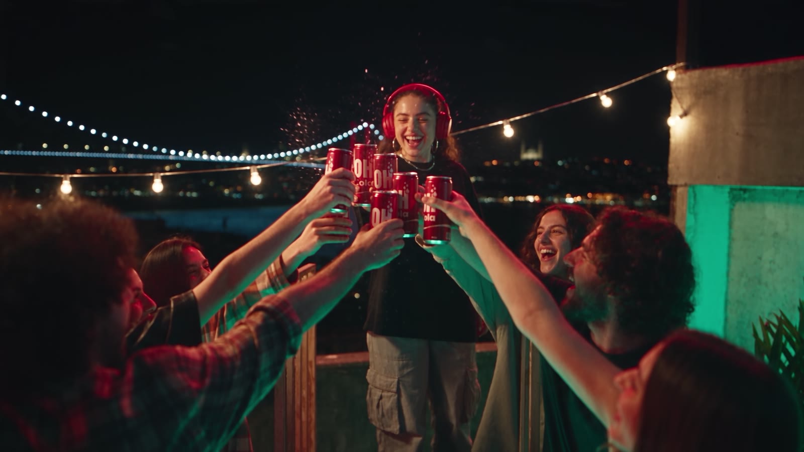 Szene aus dem KI-Werbespot OH Cola: Freunde stoßen nachts auf einer Dachterrasse an